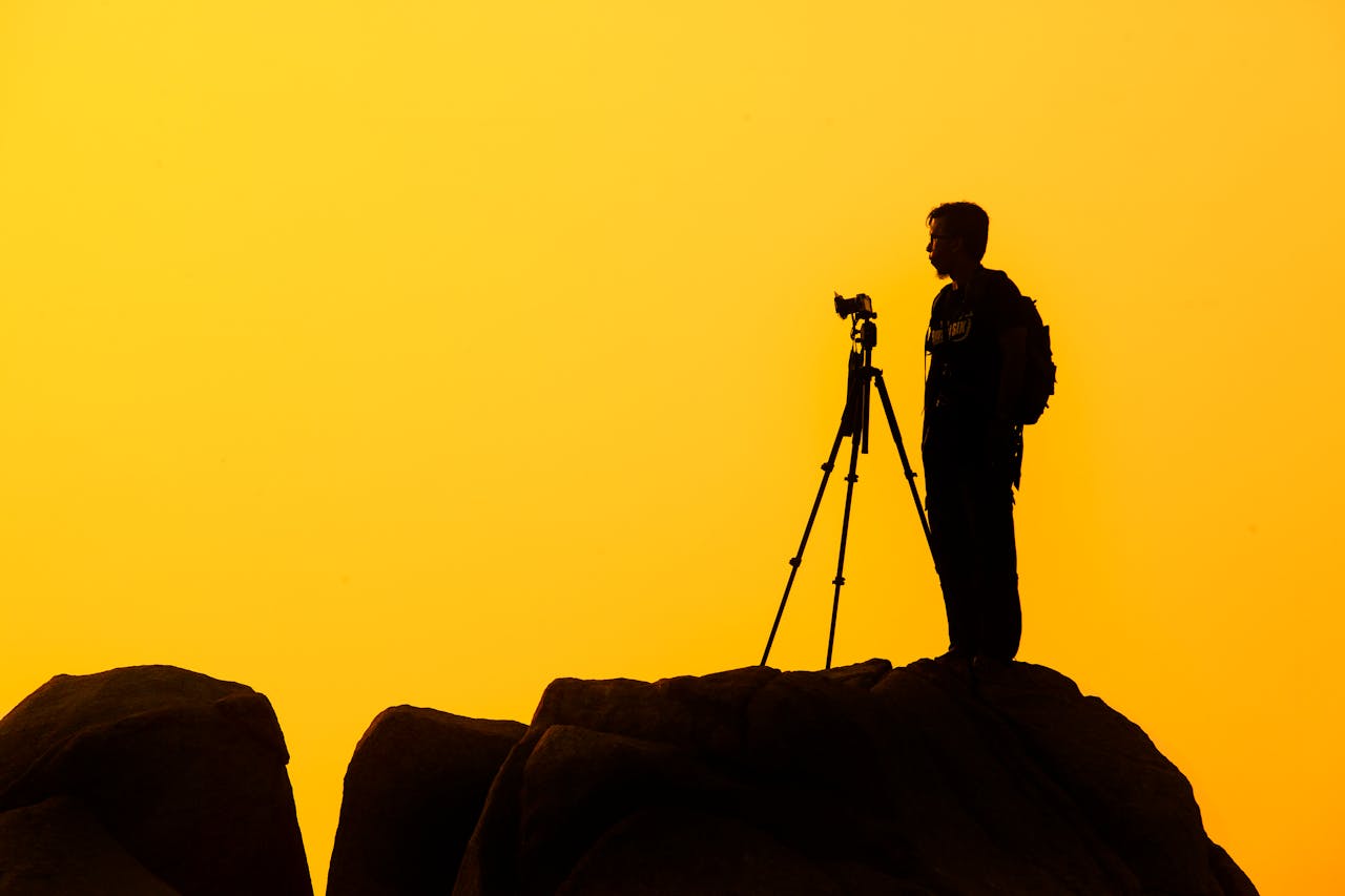 service-01 Silhouette of a lone photographer with tripod on a rocky cliff against a golden sunset sky.